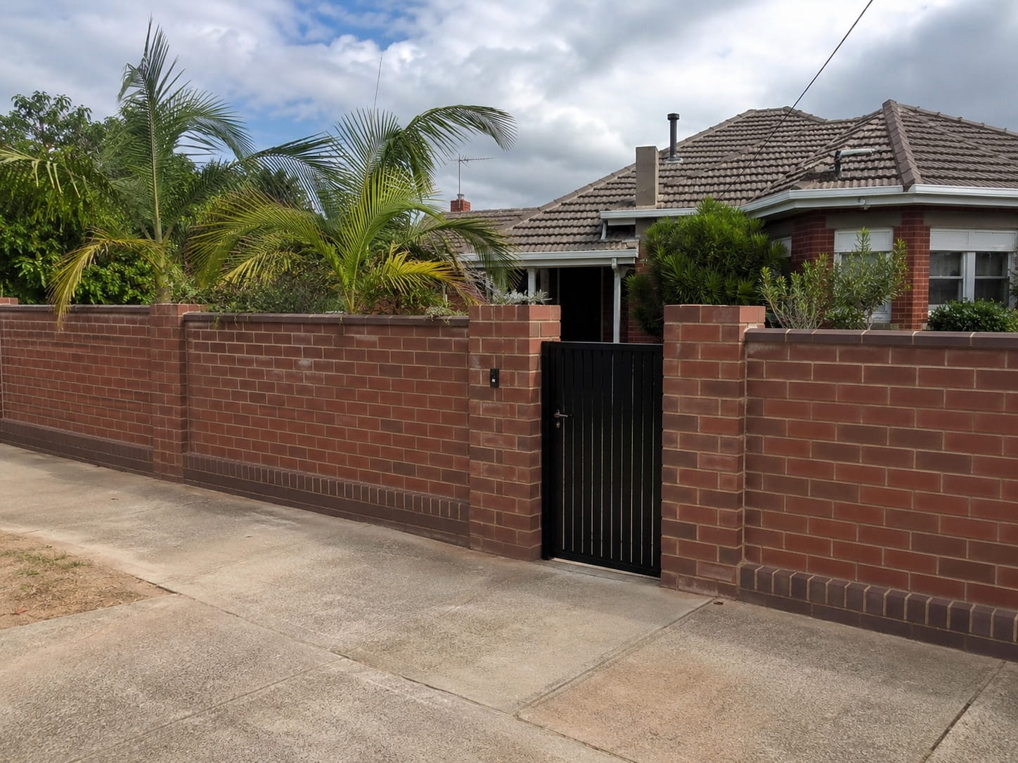Finished red brick boundary fence with a black gate and feature pillars at a Perth property